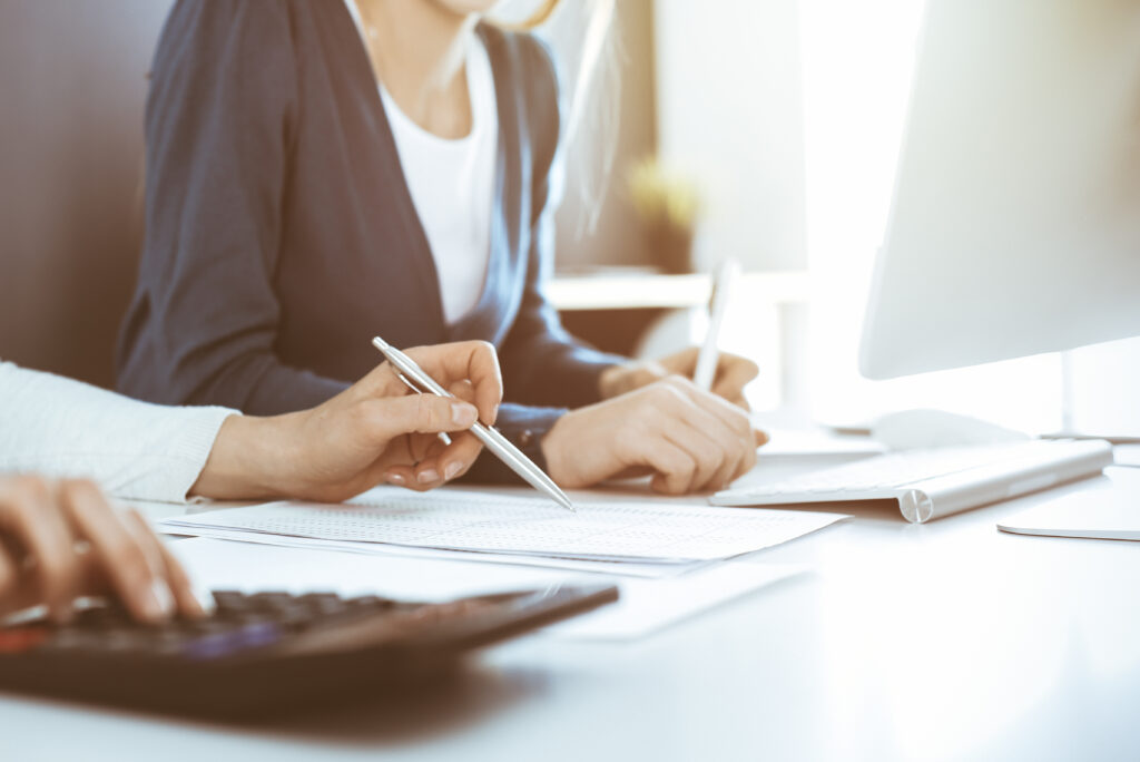Accountant checking financial statement or counting by calculator income for tax form, hands close-up. Business woman sitting and working with colleague at the desk in office. Audit concept